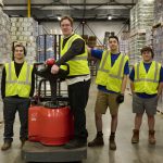 multiple warehouse workers posing with forklift in warehouse